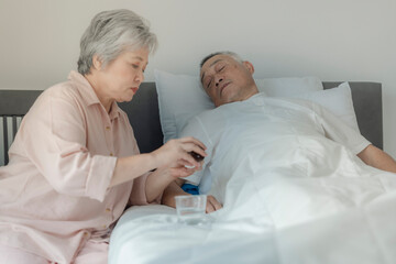 Fototapeta premium An elderly woman tends to her husband by administering medication while he rests in bed. The image emphasizes caregiving, compassion, and elderly support in a peaceful home setting.
