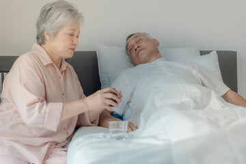 Obraz premium An elderly woman tends to her husband by administering medication while he rests in bed. The image emphasizes caregiving, compassion, and elderly support in a peaceful home setting.