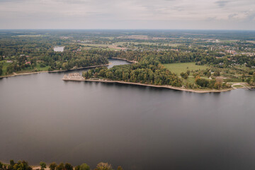 Obraz premium Aerial view of a calm lake surrounded by lush green forest and small settlements on a cloudy day..
