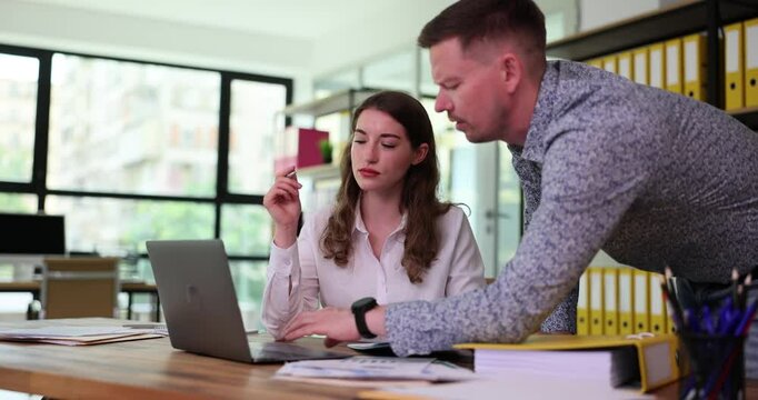Male mentor-manager overseeing trainee secretary helping colleague with computer work. Seo instructing intern to give advice at office desk