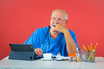 An elderly man, a doctor, in his office, at the table. Blue background.