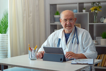 An elderly man, a doctor, in his office, at a table.