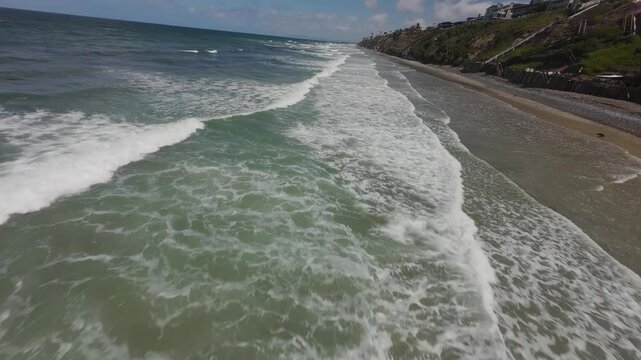 Drone footage of Moonlight State Beach with ocean waves, on a sunny day with blue sky