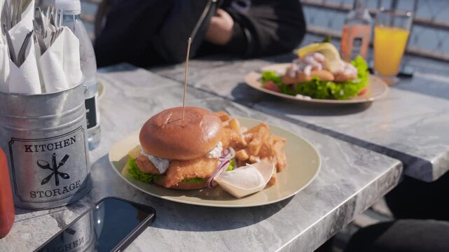 Slow zoom out of chicken burger, fries dish placed on sunny outside table