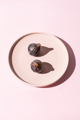 Two whole purple figs on a pink plate with light background
