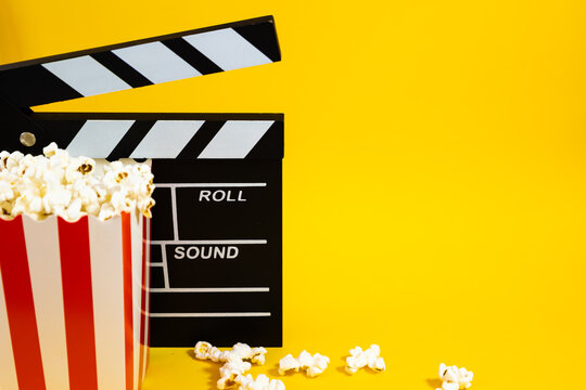 Horizontal image of popcorn with wooden clapperboard on a yellow background with popcorn scattered around, cinema and entertainment concept