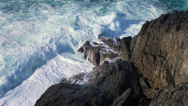stormy sea with foamy waves crashing rocky beach at Seixo Branco Near Oleiros on a sunny day