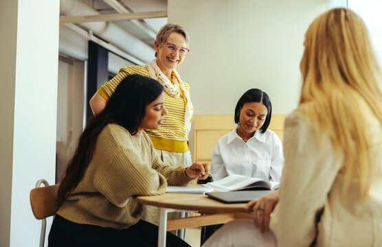 Cheerful educator engaging with a diverse group of students in a classroom setting, fostering a positive and collaborative learning environment with smiles and open discussions.