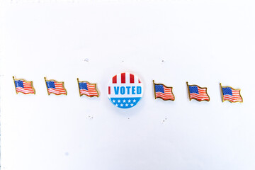 I Voted button with American flag pins in horizontal arrangement. An "I Voted" button placed in the center with six American flag pins symmetrically aligned in a horizontal row on a white background. 