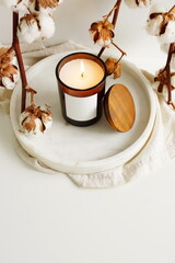 Aroma burning candle in jar blank mockup and cotton flowers on the marble tray on the table top view. Home cozy interior decoration, copy space.