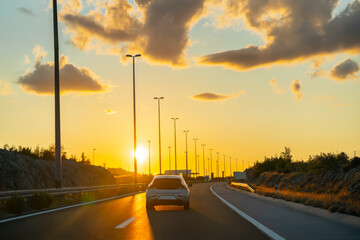 Cars are driving along the highway. The highway is illuminated golden with the light of the setting sun. Concept of traveling by car, transportation, logistics 
