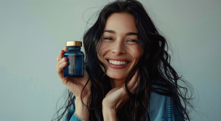 A beautiful luxury 35+ age woman with long dark hair smiling and holding up an empty dark blue glass supplement bottle against a white background