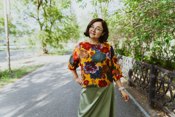 Joyful young Asian woman enjoying a walk on a summer sunny day in the park. Asian woman with a joyful, open smile enjoys the tranquility of a summer day while walking along the sidewalk of a park