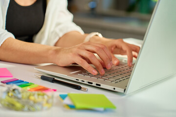 Woman working from home office typing on laptop keyboard with colorful sticky notes and stationery on desk