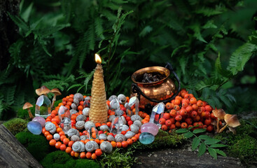 candle, witch cauldron, crystals and spiral made of snail shells and rowan berries in forest....