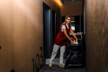 Happy chambermaid cleans and throws away dirty towels from the hotel room.
