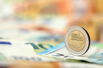 Two euro coin lies on huge amount of different euro dollars banknotes