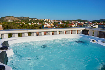 Outdoor hot tub on sunny rooftop deck with bubbling water and comfortable seating with beautiful view on touristic cityscape. Place for relaxation and leisure during summer vacations