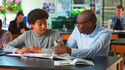 Male High School Student Receiving Individual Attention From Teacher In Science Class