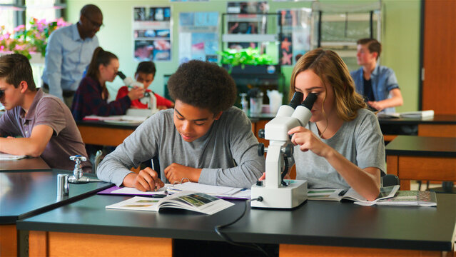 Male And Female High School Students Using Microscope In Biology Class