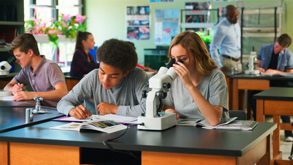 Male And Female High School Students Using Microscope In Biology Class