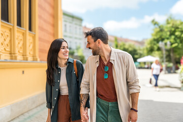 Young happy couple in love exchanging looks in the city street. Man and woman, people in relationship outdoor. Modern alternative carefree couple travelers and tourists vacation destination.