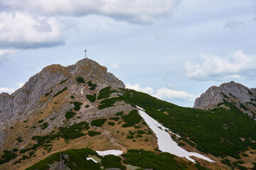 Fototapeta premium Rugged hiking trail leading to mountain summit with large cross under cloudy sky. Tatra mountains in Zakopane, Poland. Giewont mountain summit. Natural landscape