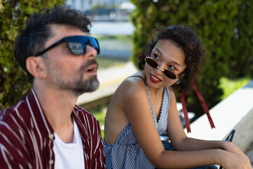 Obraz premium Casual outdoor conversation between two friends wearing sunglasses on a sunny day, enjoying a relaxed moment in an urban setting