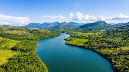 Obraz premium A serene view of a winding river surrounded by lush green hills under a bright blue sky.
