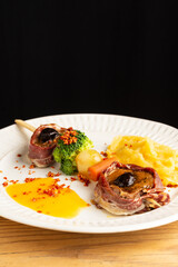 Top view of sirloin skewer with broccoli, carrot, potato and sauce, on white plate, black background, vertical, with copy space