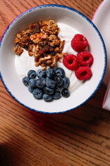 A bowl of yogurt parfait with granola, raspberries, and blueberries.