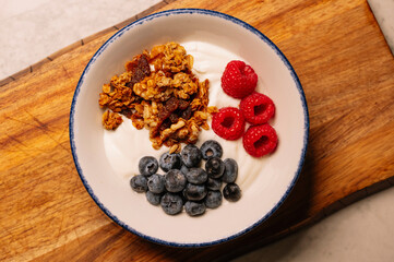 A bowl of yogurt parfait with granola, raspberries, and blueberries.