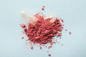 Opened cranberry Vaccinium Oxycoccus gel capsule with red vitamin powder spilled out. Blue studio...