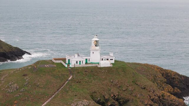 Strumble head lighthouse aerial view orbiting stone tower on Pembrokeshire rugged coastal mainland