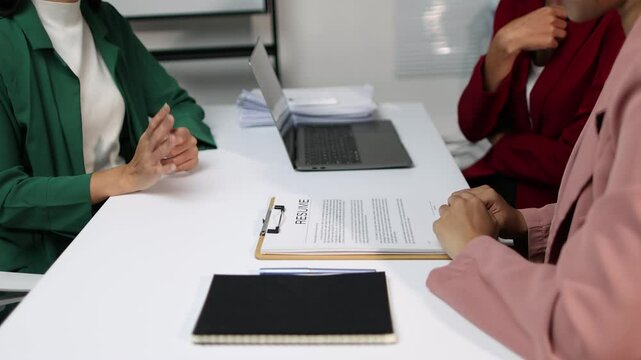 Asian businesswoman interviewing candidate for job position. Applicant in a green jacket participate in a job interview with two hr managers. They engage in conversation while seated at desk in office