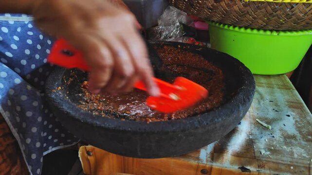 A female chef makes manual peanut sauce using a stone mill