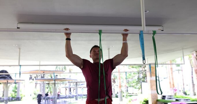 Young man pulls up on horizontal bar with elastic band outdoors. Concept of fitness sport exercise training and lifestyle