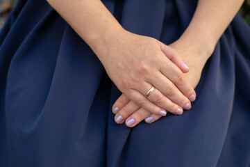 part of a female body, female hands with a ring on an elegant blue skirt, female hands aged 40-45 years