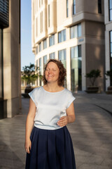 Fototapeta premium woman with curly short hair smiles and looks at the camera, close-up, half-length portrait in the city of a woman 40-45 years old 