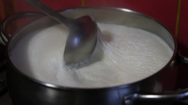 Milk boils and steams hot. Boiling milk in a stainless steel vessel. The milk is about to boil. Boiling milk flows from the pan onto the gas stove. Cow's milked boils in a kettle. 4K