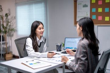 Two businesswomen discussing financial charts and data on a desk in the office