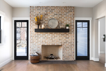 A natural fireplace detail with decorations on a wooden shelf, black framed windows, and a hardwood...