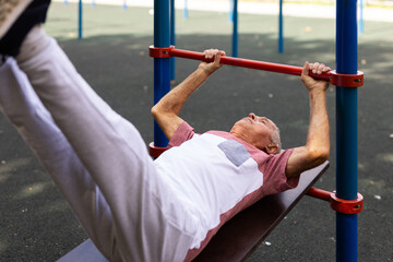 Open air gym. Street training on the municipal sports equipment. Elderly man pumps the press in city park