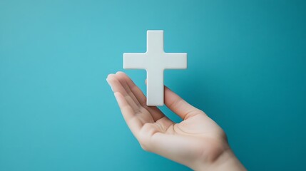 Obraz premium A hand holding a white cross against a blue background.