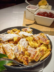 Famous Austrian sweet dish Kaiserschmarrn served in a pan with ice cream, raspberry and stewed plums
