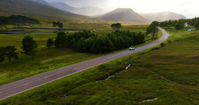 White electric car driving in the Highlands in Scotland route in beautiful Scottish landscape.