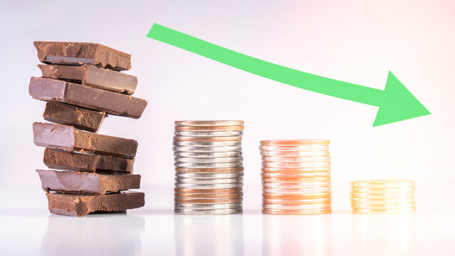 A stack of chocolate bars and a pile of coins are shown, with the coins being smaller and more numerous than the chocolate bars. Concept of a decrease in value