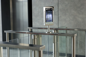 A metal gate with a green light on electronic turnstiles with A security camera.