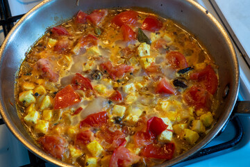 Paneer or Indian cottage cheese cubes cooking Indian style with tomato and spices in a frying pan. Spicy vegetarian curry.