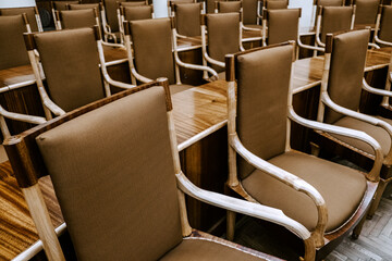 Fototapeta premium Rows of empty wooden chairs with fabric upholstery in a conference room, meeting or seminar setting, classic interior design